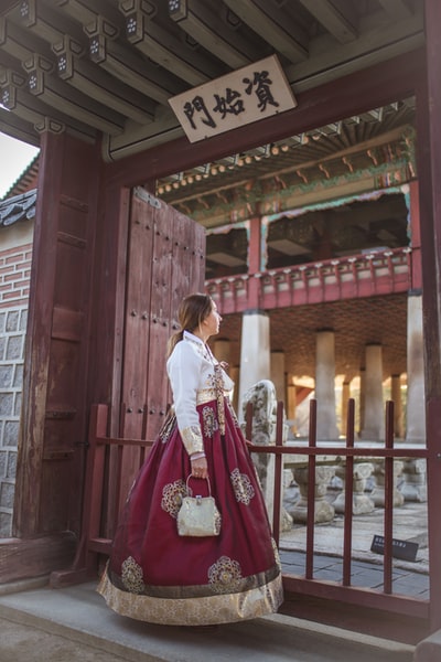 白天，穿着白色长袖衬衫和红色裙子的女人站在棕色的木门旁